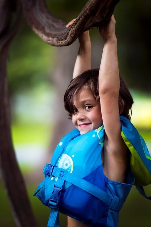 Child in a life jacket hanging on to a tree limb